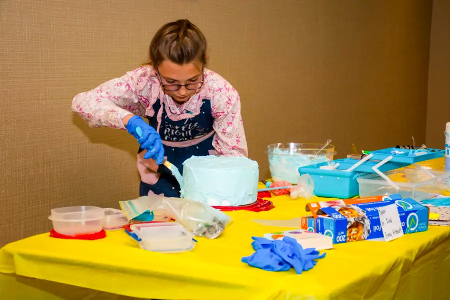 a girl is surrounded by bowls as she frosts a cake with teal frosting