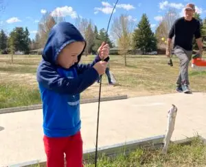 a boy holds a fishing pole while a fish he caught dangles from the end of the line