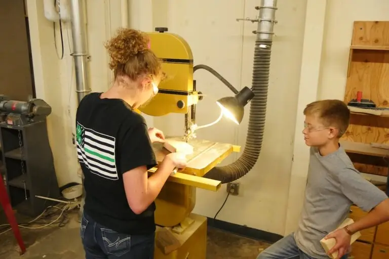 a girl cuts a pattern on a band saw while a boy watches