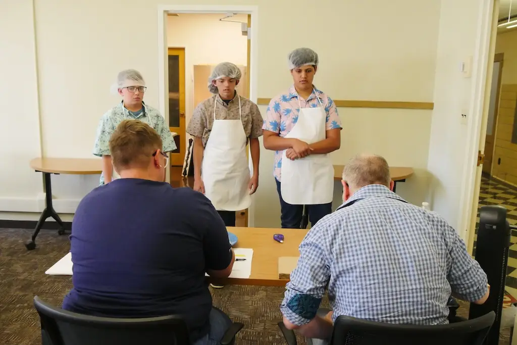 three young people face a panel of two judges and explain the food they've prepared