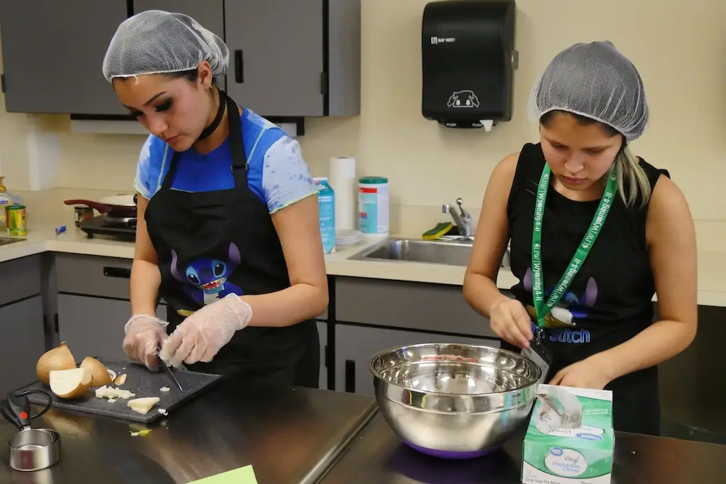 two young people stand next to each other at a counter cutting ingredients and mixing food in bowls