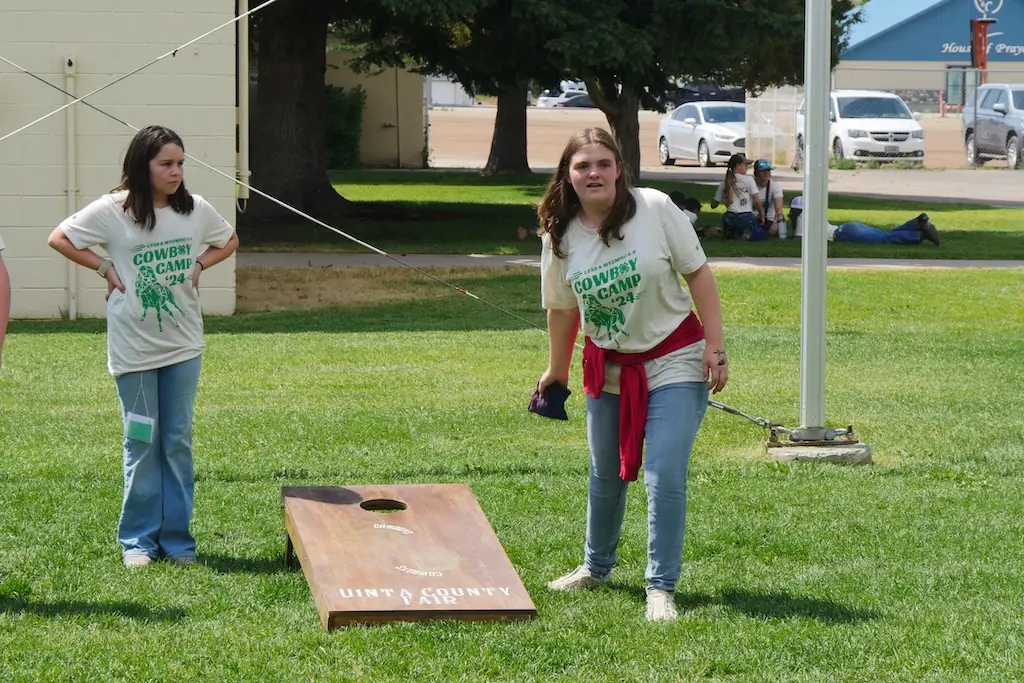 two girls play cornhole, one is in the middle of throwing