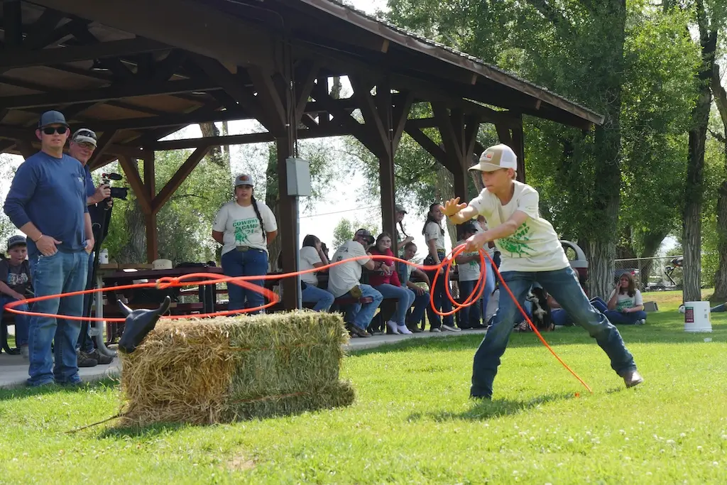 A youth throws a rope around a straw bale calf while a small crowd watches
