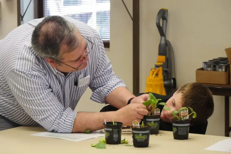 an adult leader helps a youth graft a leaf on a potted plant