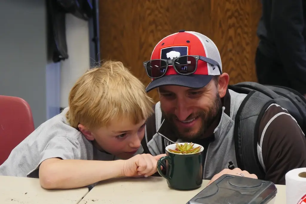 A child and an adult volunteer look closely at a cactus planted in a mug