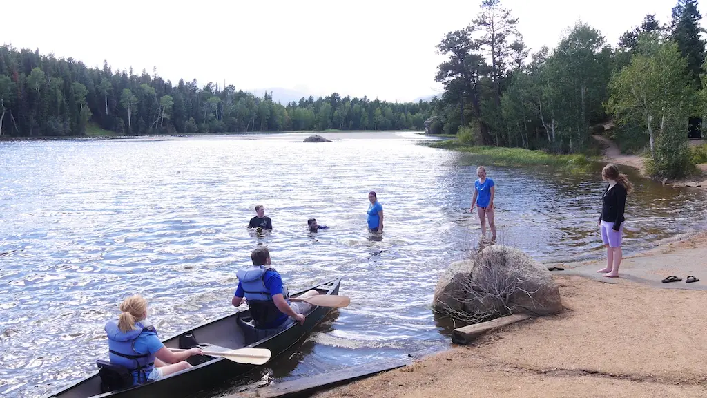 a group of youth at a lake, some in the water a two others in a canoe