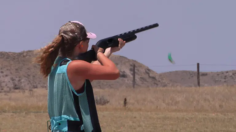 a young woman holds a shotgun to her shoulder waiting for a clay to be released