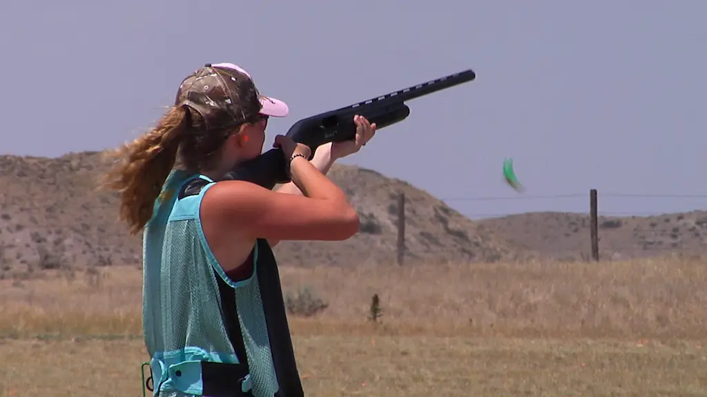 a young woman holds a shotgun to her shoulder waiting for a clay to be released