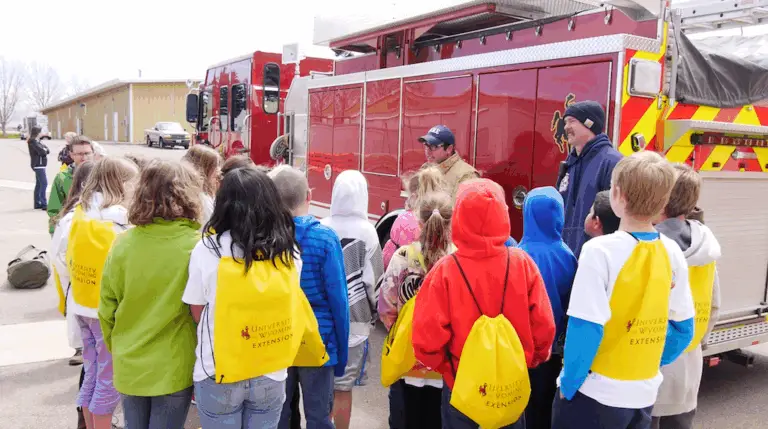 a group of young people gather around a fire truck while a fire fighter explains some of the tools they use