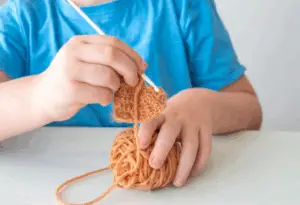 close up of hands and arms crocheting and heart shape with brown yarn