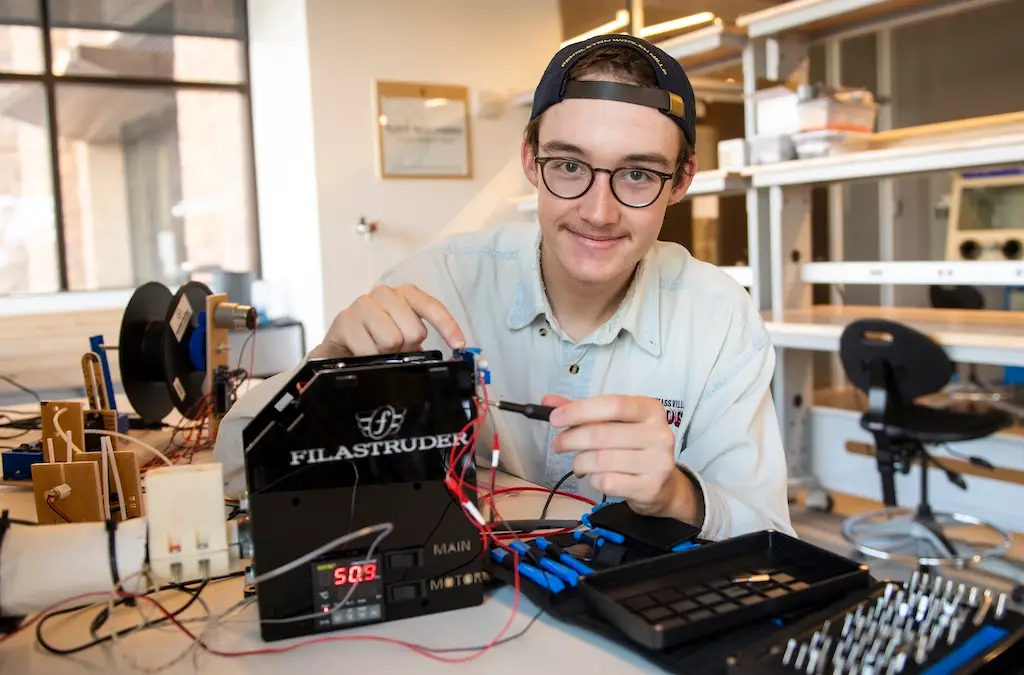 a young man touches a probe to an electronic instrument on a table in a lab