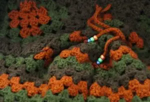 closeup of a crochet project made of striped bands of green and orange thread
