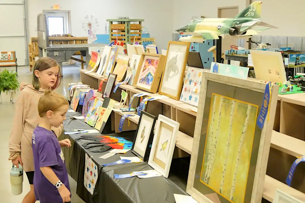 two children look at painting and art projects displayed on a table at the fair