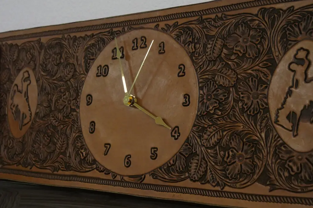 a tooled leather wall clock with a bucking horse on it