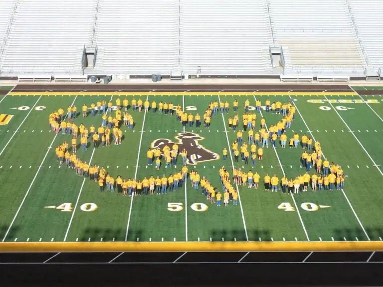 a group of people wearing gold shirts stand on a football field in the shape of a 4-H clover