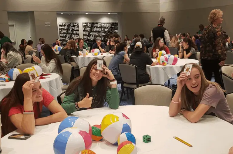 young people, one showing thumbs up and smiling hold cards on their foreheads while playing a game at a conference