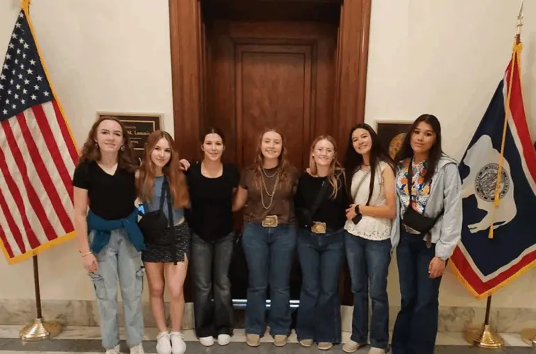 a group of young people stand in front of a door flanked by a US and Wyoming flag