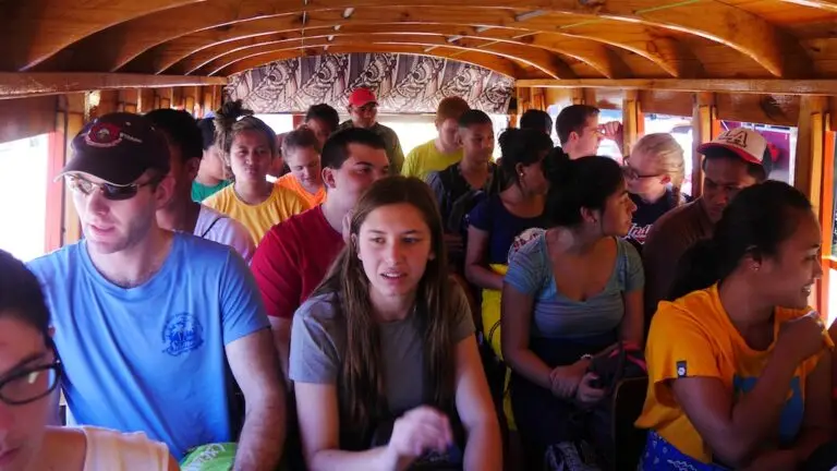a group of young people and chaperone sit close together riding in a small bus with wood paneling
