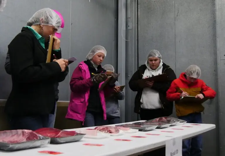 a group of young people with clipboards gather around a table studying packages of meat