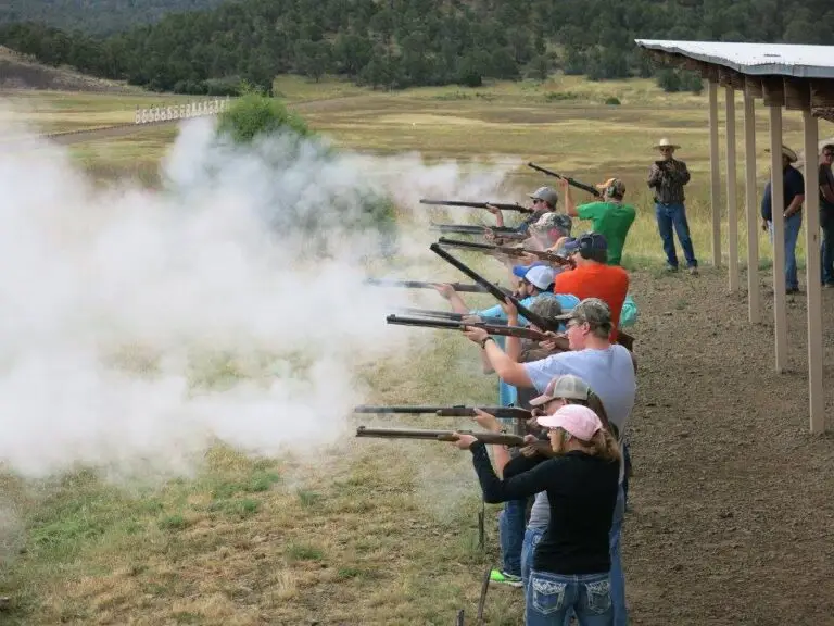 a line of young people fire shotguns at the same time with smoke visible from the barrels