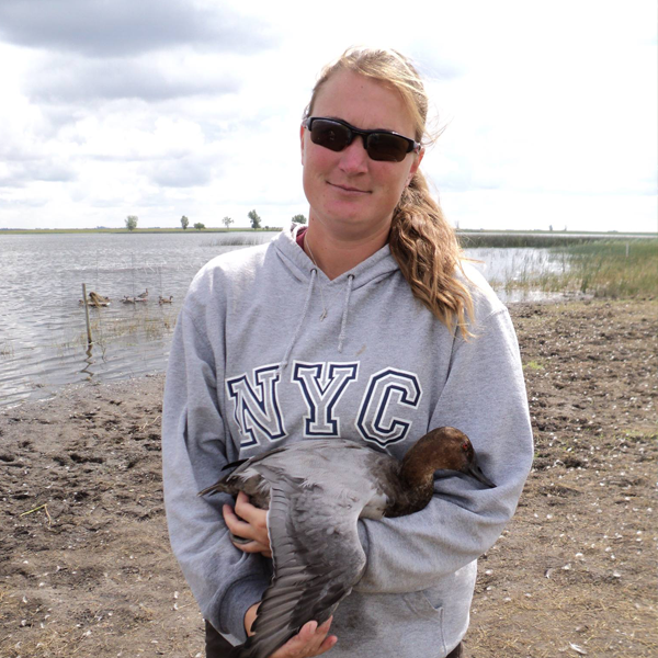 amie Allen in a grey sweatshirt holding a waterfowl in front of a serene lake